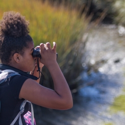 African American child using binoculars by a creek