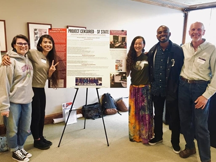 group of student and teacher standing in front of a poster presentation